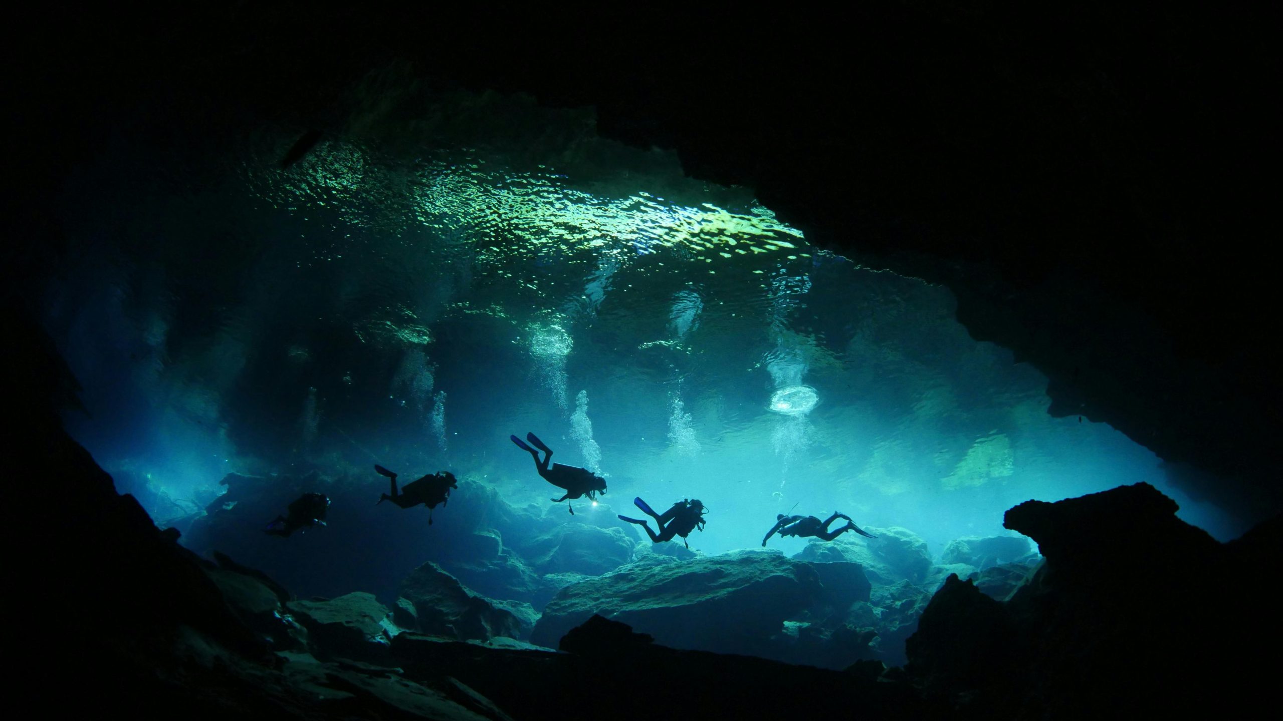 A group of divers explores a mysterious underwater cave with fascinating rock formations.